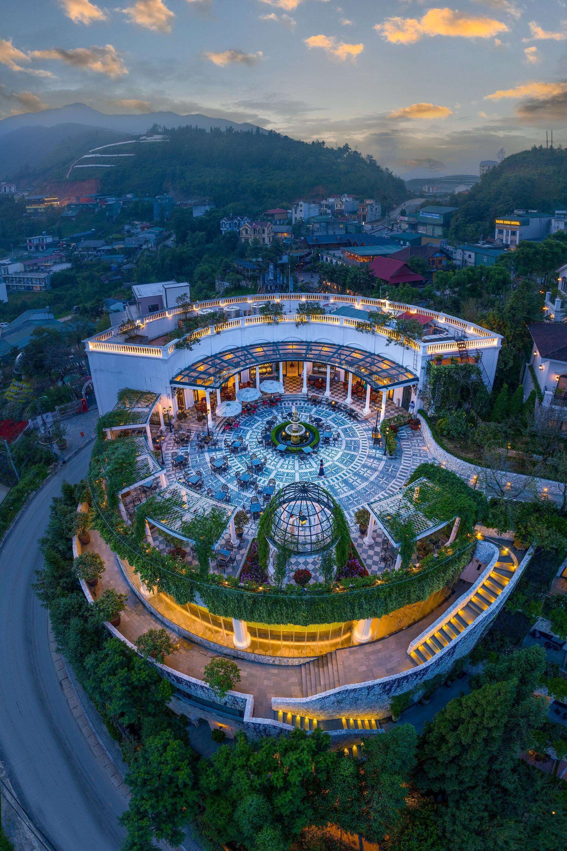 A circular hotel with a central courtyard, surrounded by lush greenery and a winding road.