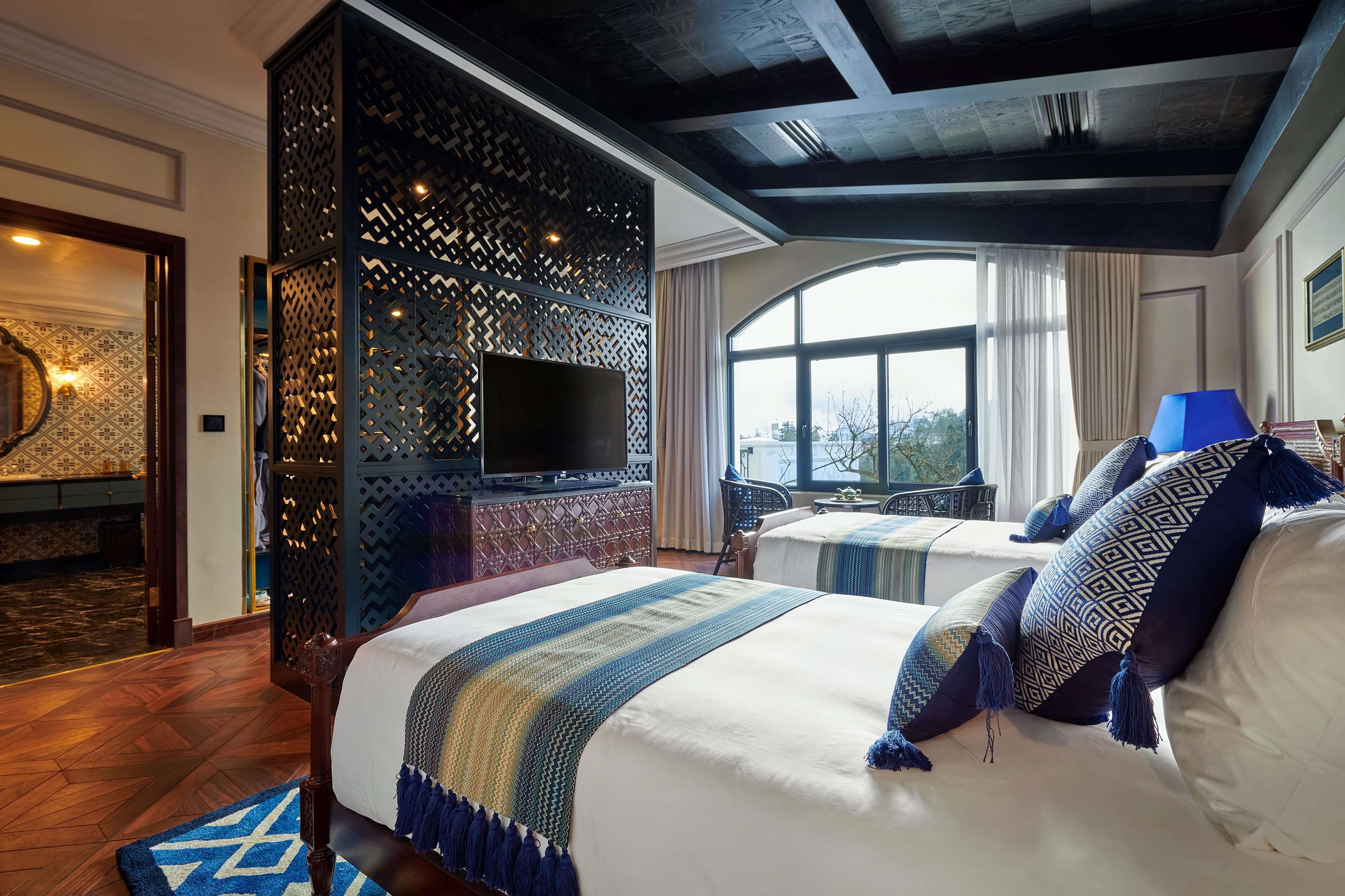A hotel room with two beds, a TV, and a view of the outdoors.