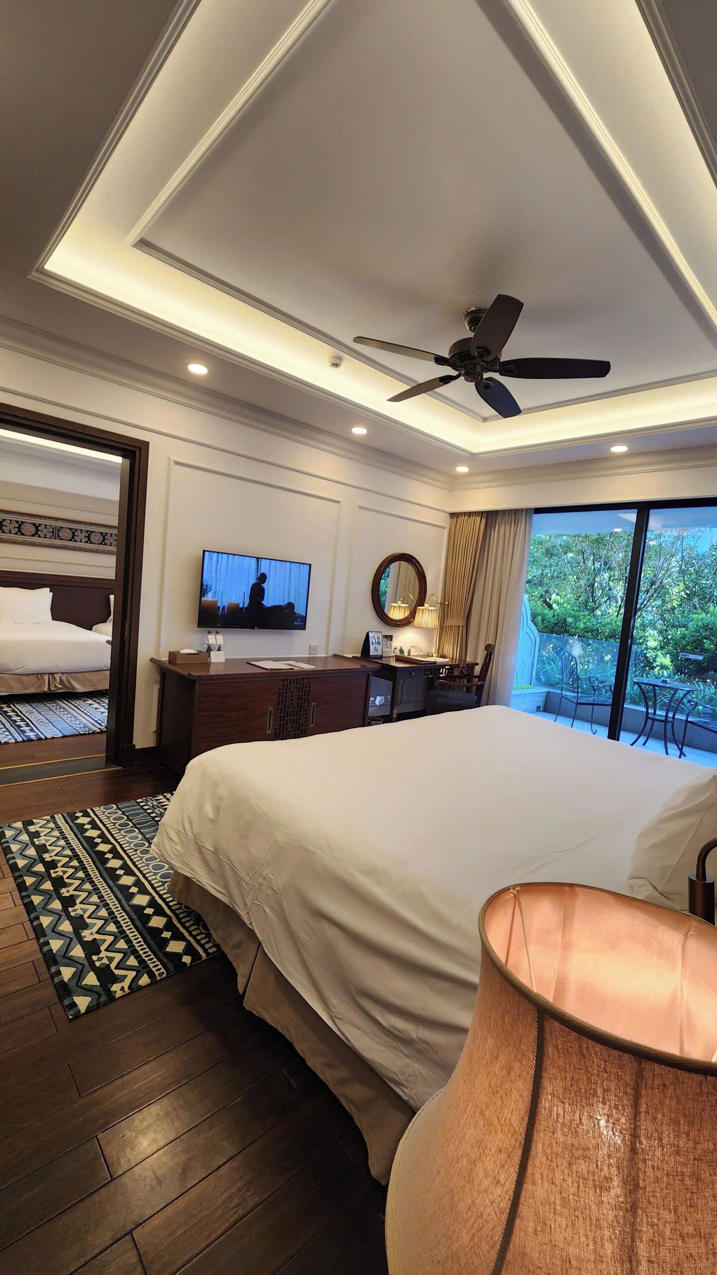 Habitación de hotel con una cama grande, un escritorio con silla, un televisor, un ventilador de techo y vistas al exterior.