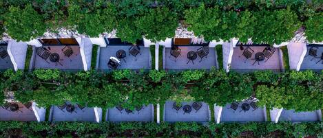 A rooftop garden with multiple seating areas, each with a table and chairs, surrounded by lush greenery.