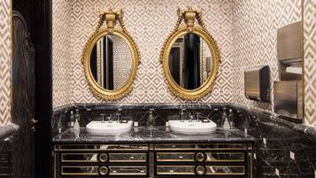 A luxurious bathroom with a black and gold vanity, two gold-framed mirrors, and a marble floor.