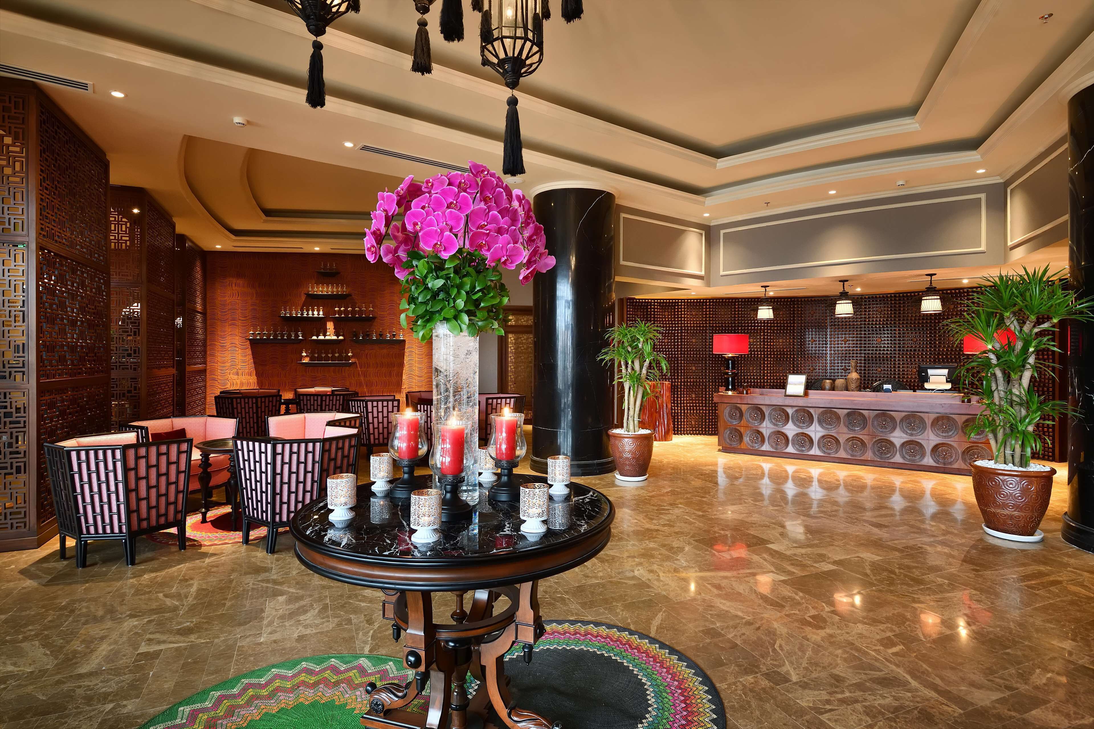 A lobby with a reception desk, seating area, and decorative elements like a vase of flowers and candles.