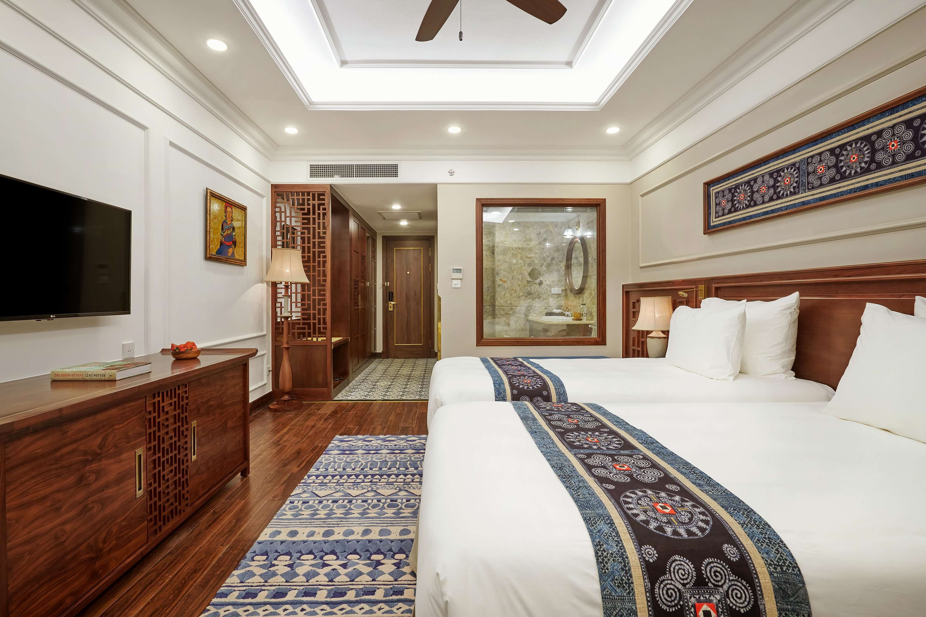 Habitación de hotel con una cama grande, televisor, mueble de madera y alfombra estampada.