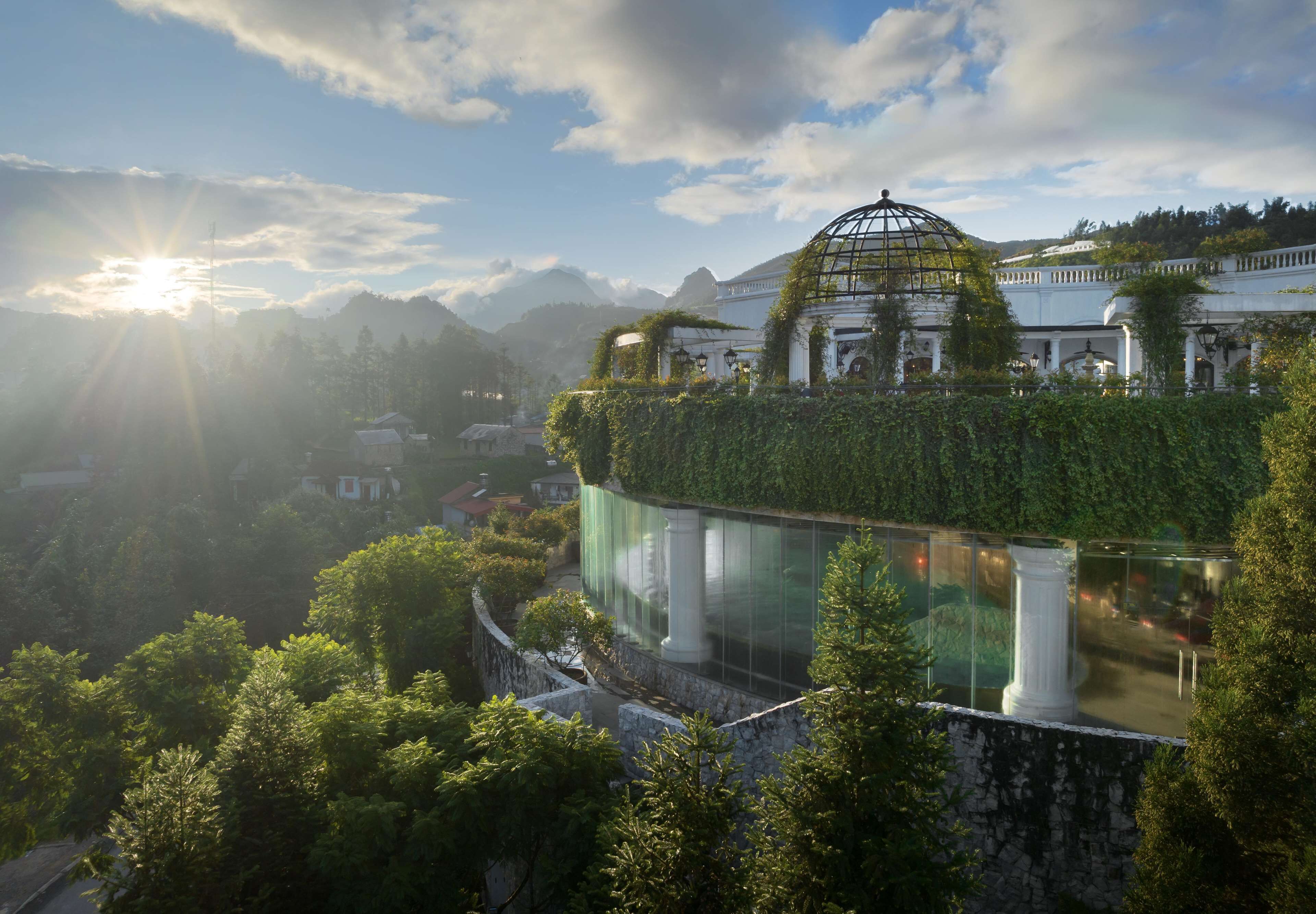 Um edifício clássico com cúpula, rodeado por vegetação exuberante e montanhas.