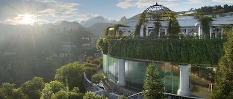 Um edifício clássico com cúpula, rodeado por vegetação exuberante e montanhas.