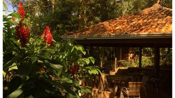 A covered outdoor area with a tiled roof, surrounded by lush greenery and red flowers.