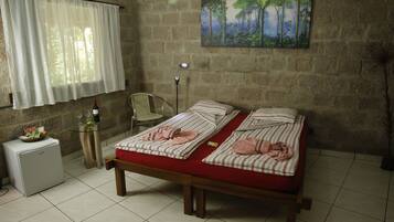 Un dormitorio con cama, refrigerador pequeño, silla, mesa y un cuadro en la pared.