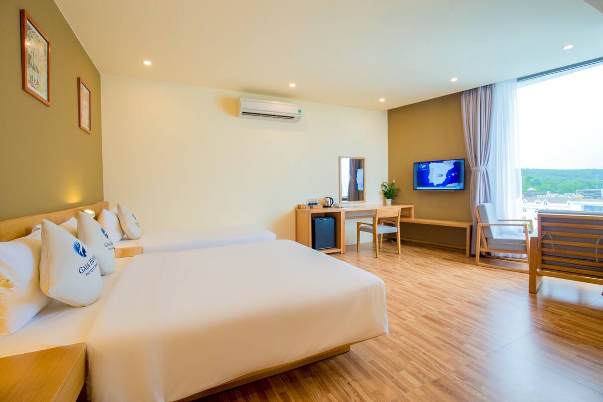 A hotel room with a large bed, a desk, a chair, a television, and a view of the city.