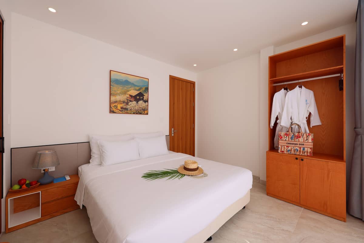 A bedroom with a bed, a nightstand, a wooden wardrobe, and a painting on the wall.