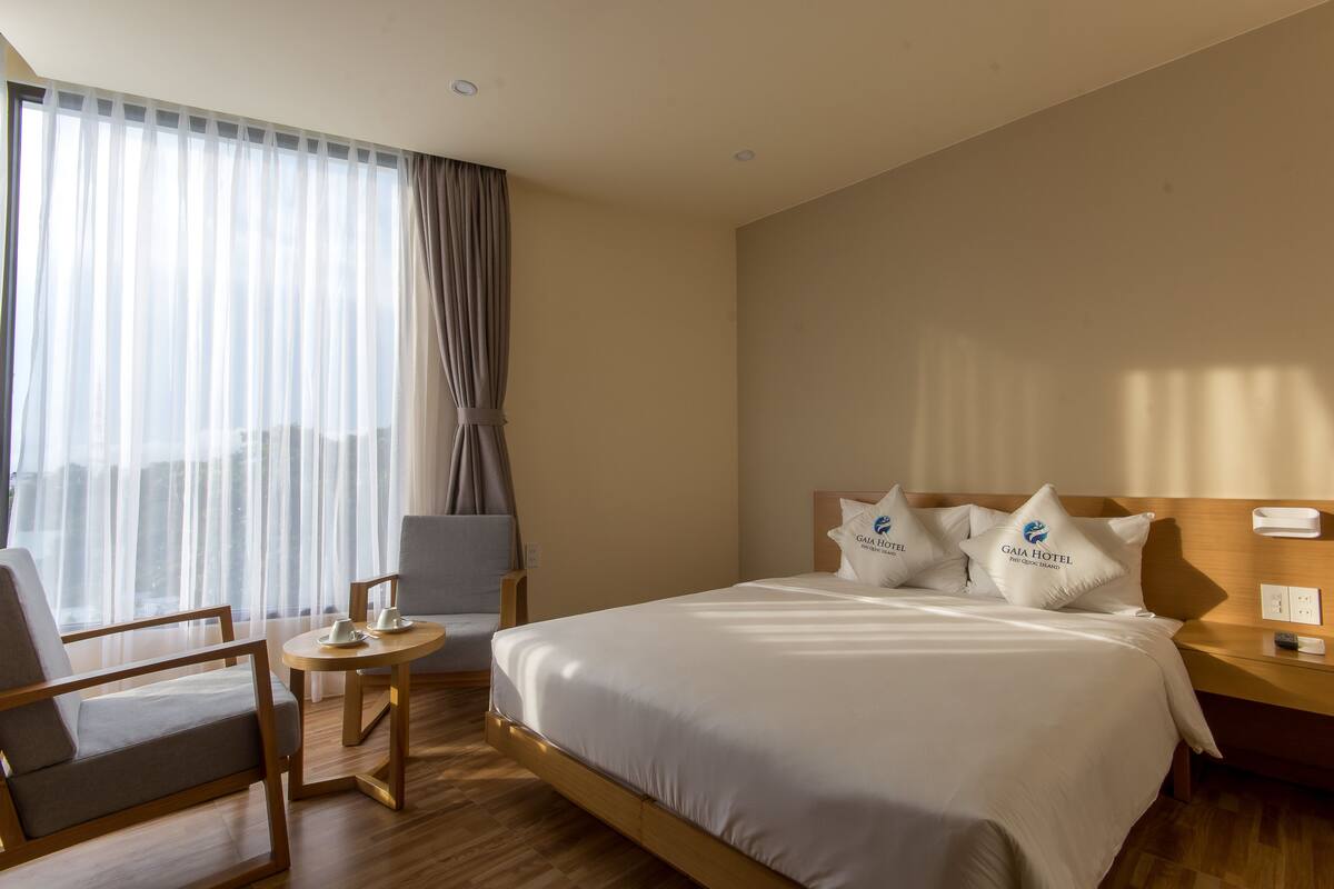 A hotel room with a bed, a chair, a small table, and a nightstand.