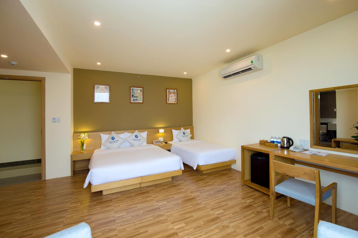 A hotel room with two beds, a desk, a chair, a mirror, and a small table with a kettle and cups.