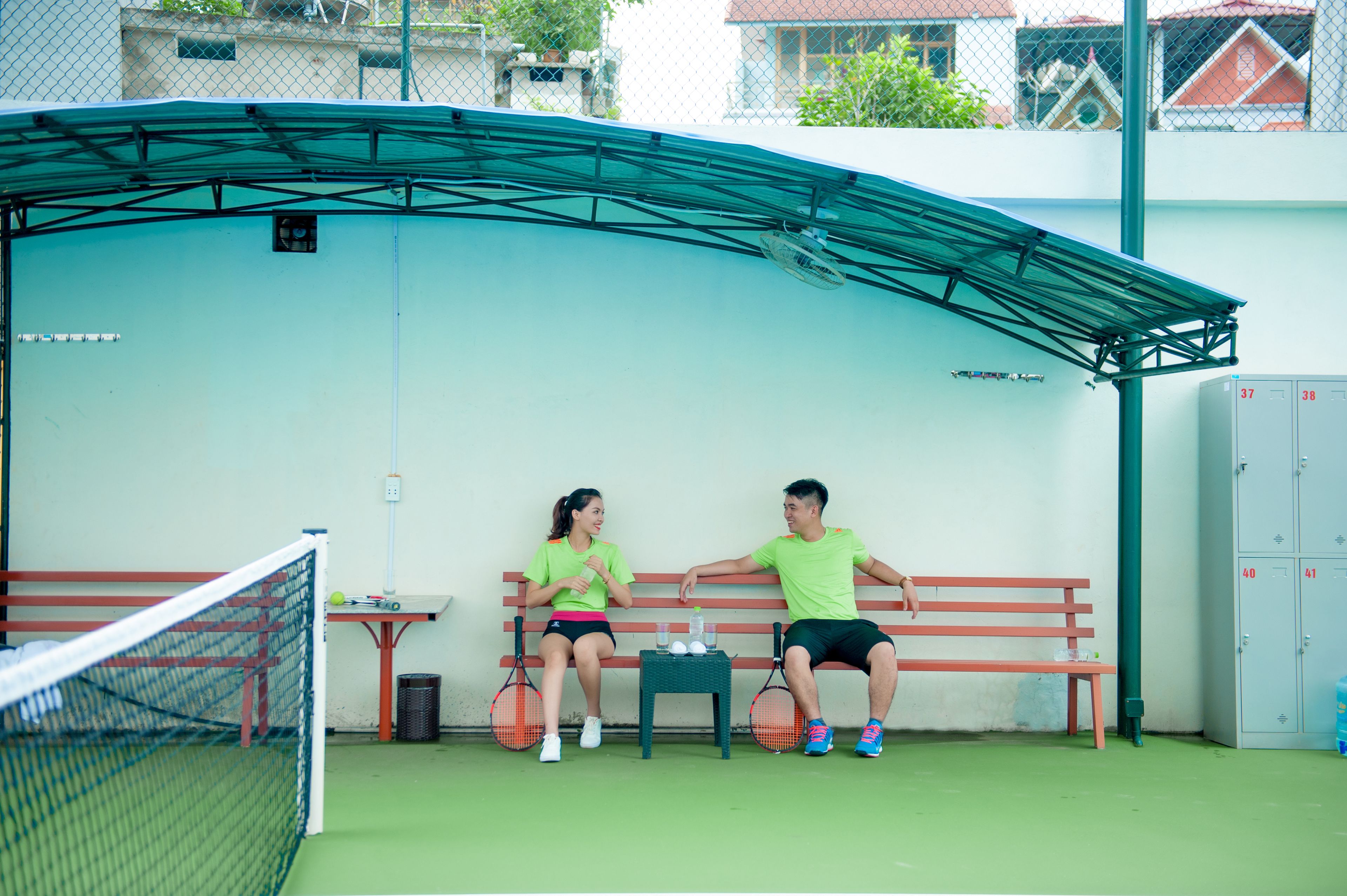 A tennis court with a net, a bench, and two people sitting on it.