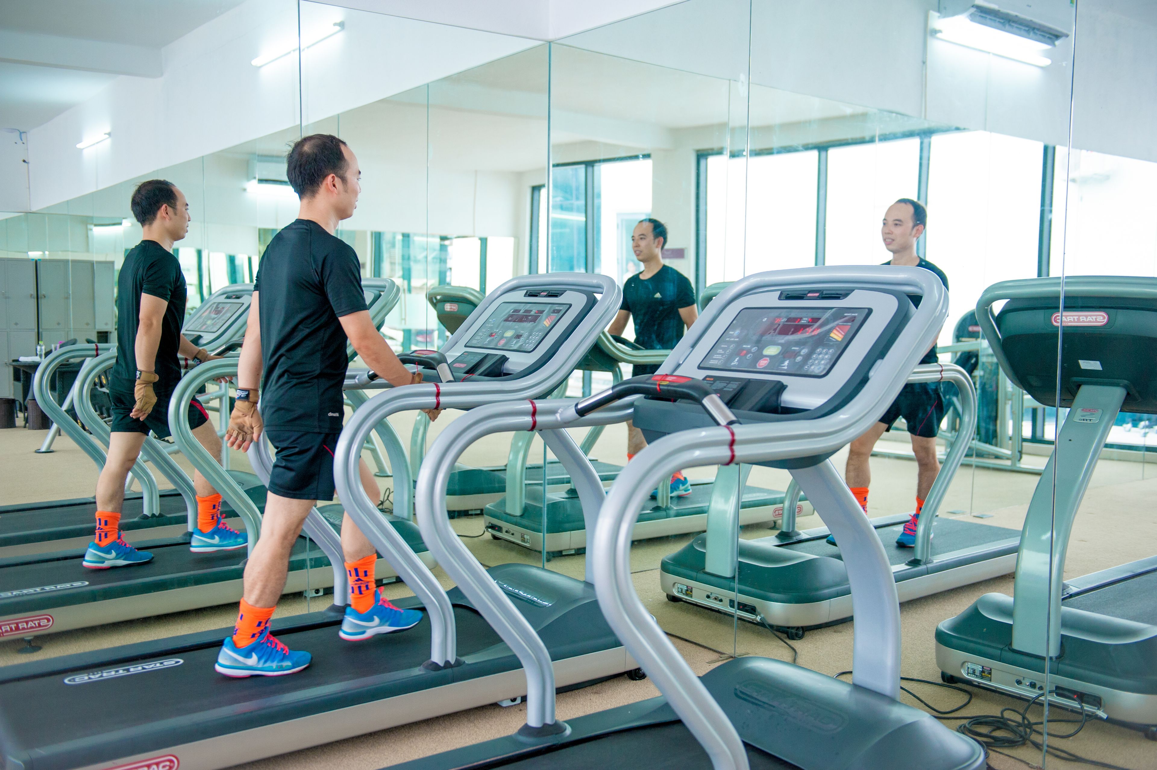 A gym with treadmills, mirrors, and a person using one.