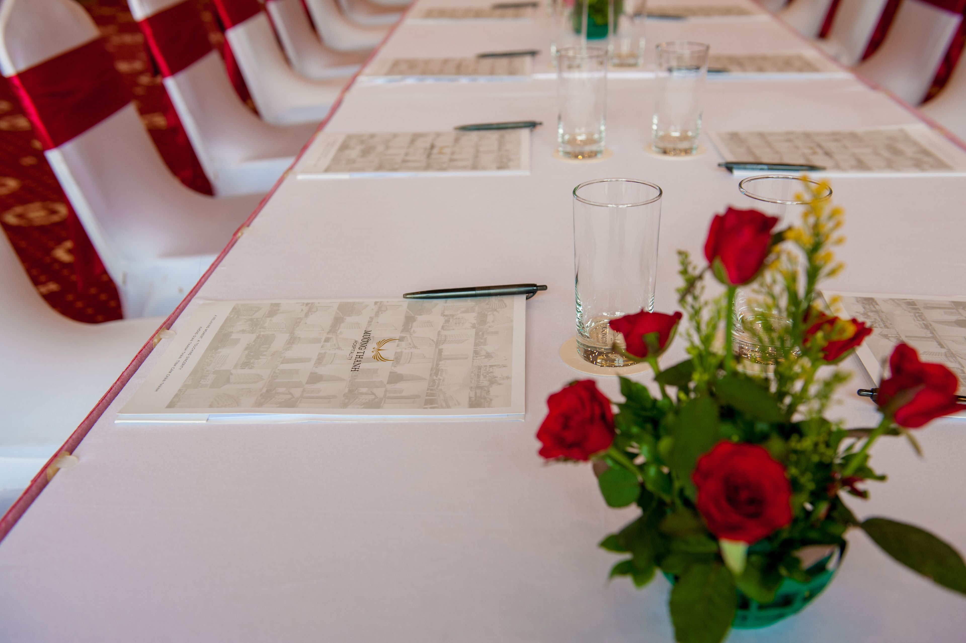 Une table de conférence avec des documents, des stylos et un vase contenant des roses rouges.