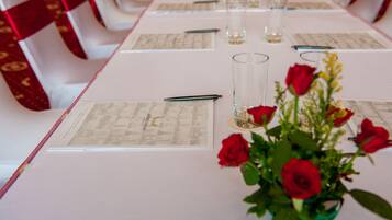 Une table de conférence avec des documents, des stylos et un vase contenant des roses rouges.