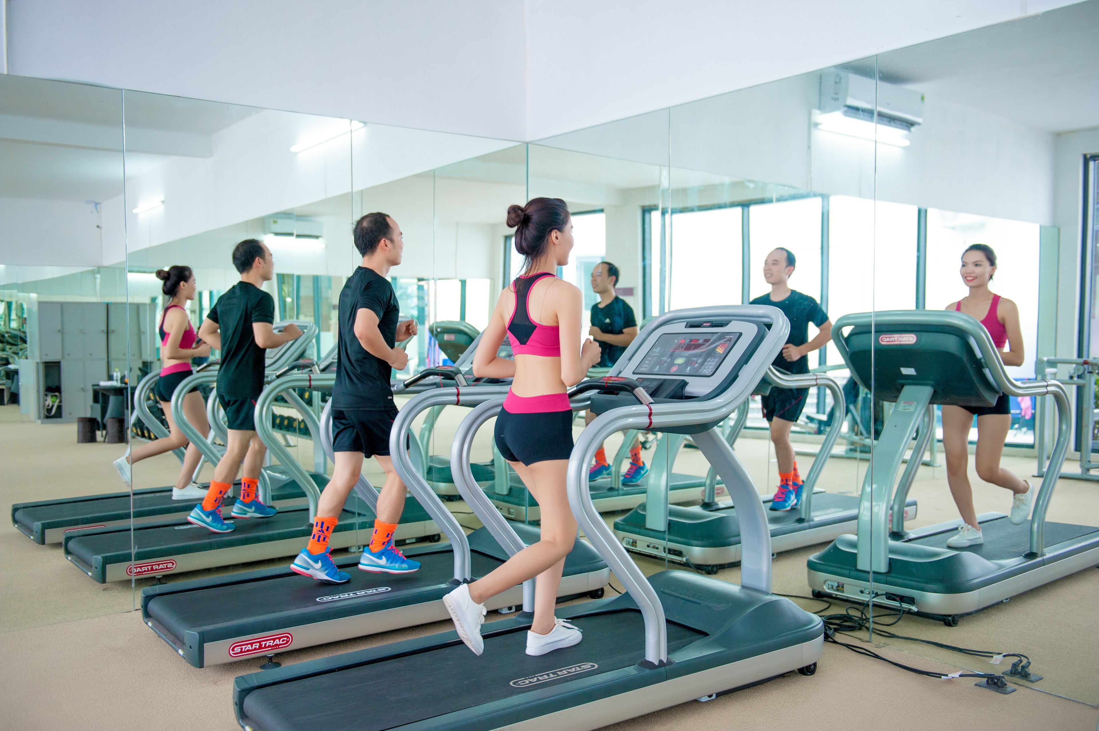 Un gimnasio con cintas de correr, espejos y equipo de ejercicio.