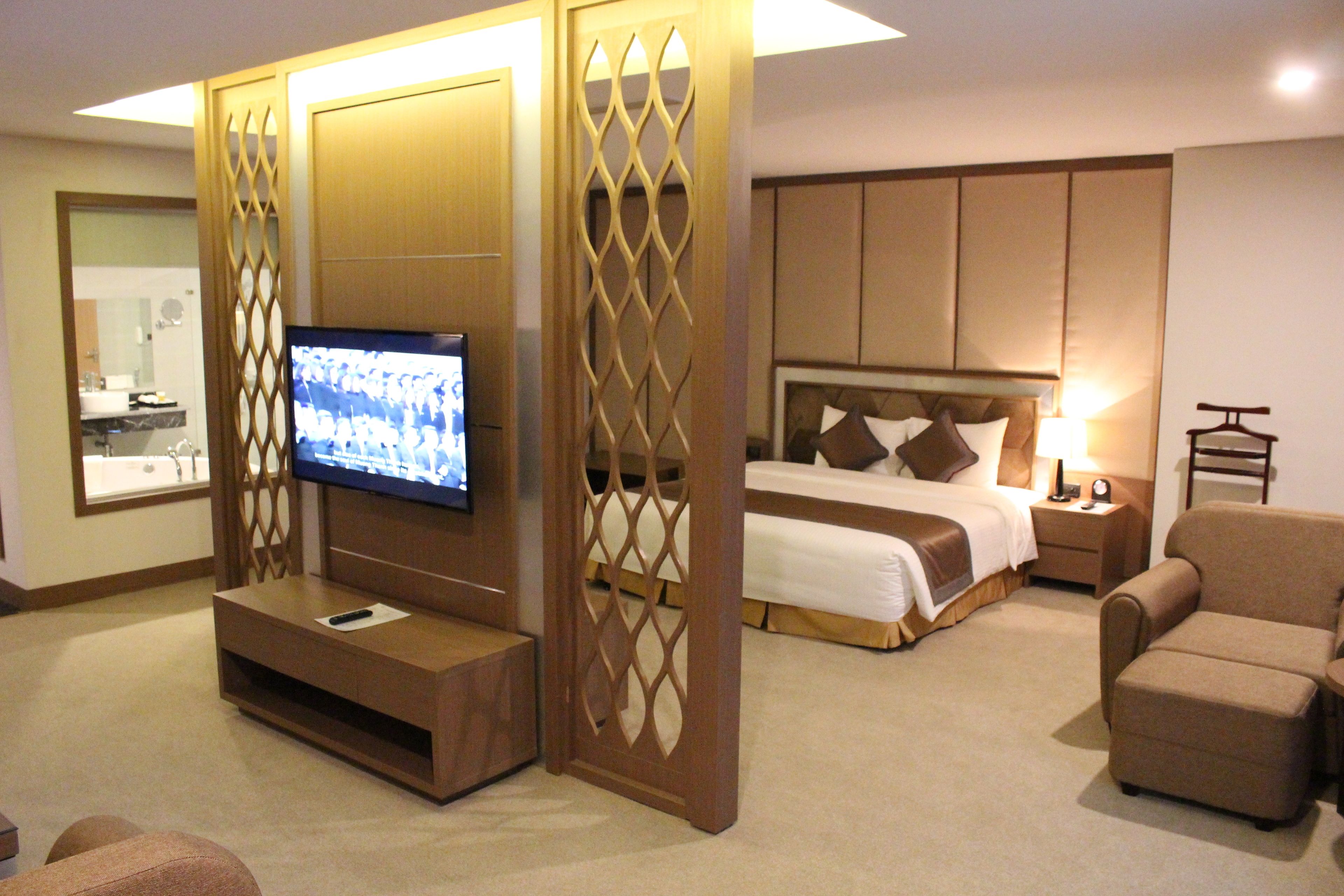 A hotel room with a TV, a bed, a nightstand, and a seating area.