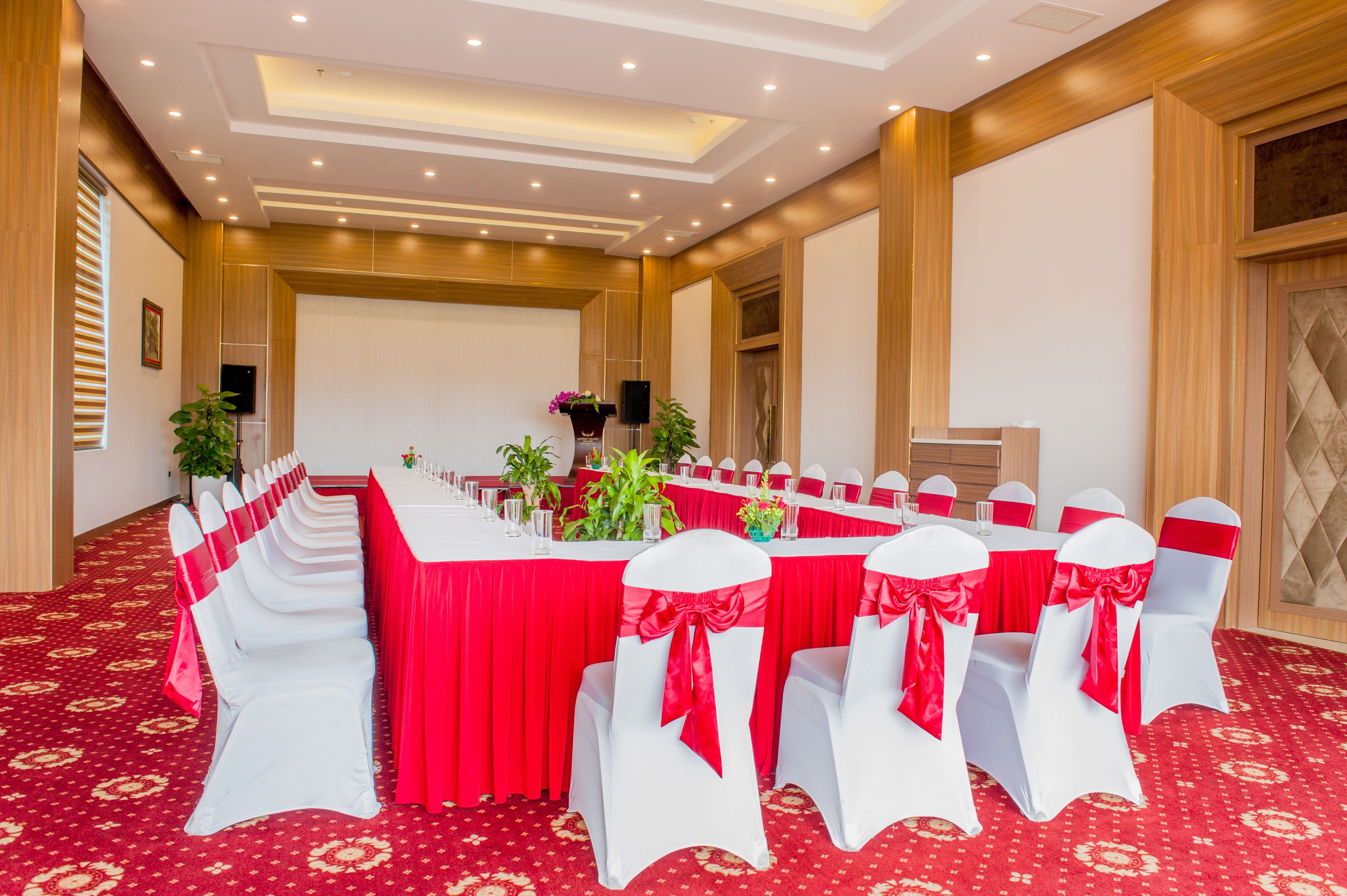 A conference room with a long table, white chairs with red sashes, and a red carpeted floor.