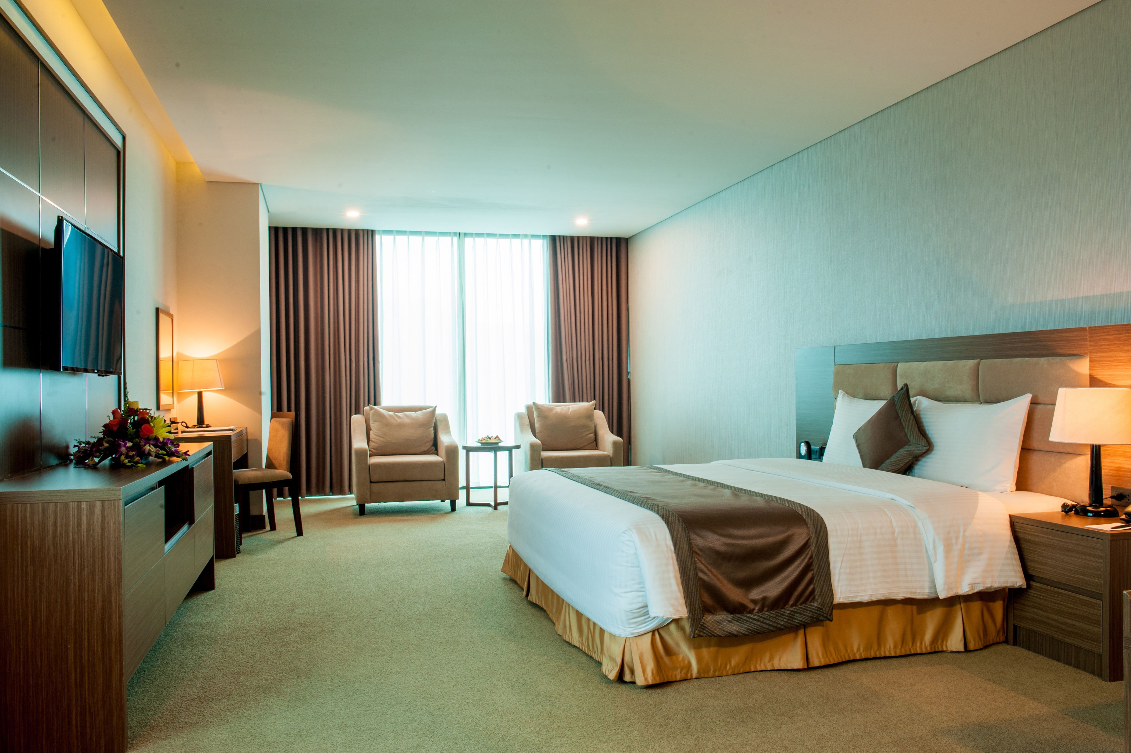 A hotel room with a large bed, two armchairs, a desk, and a TV.