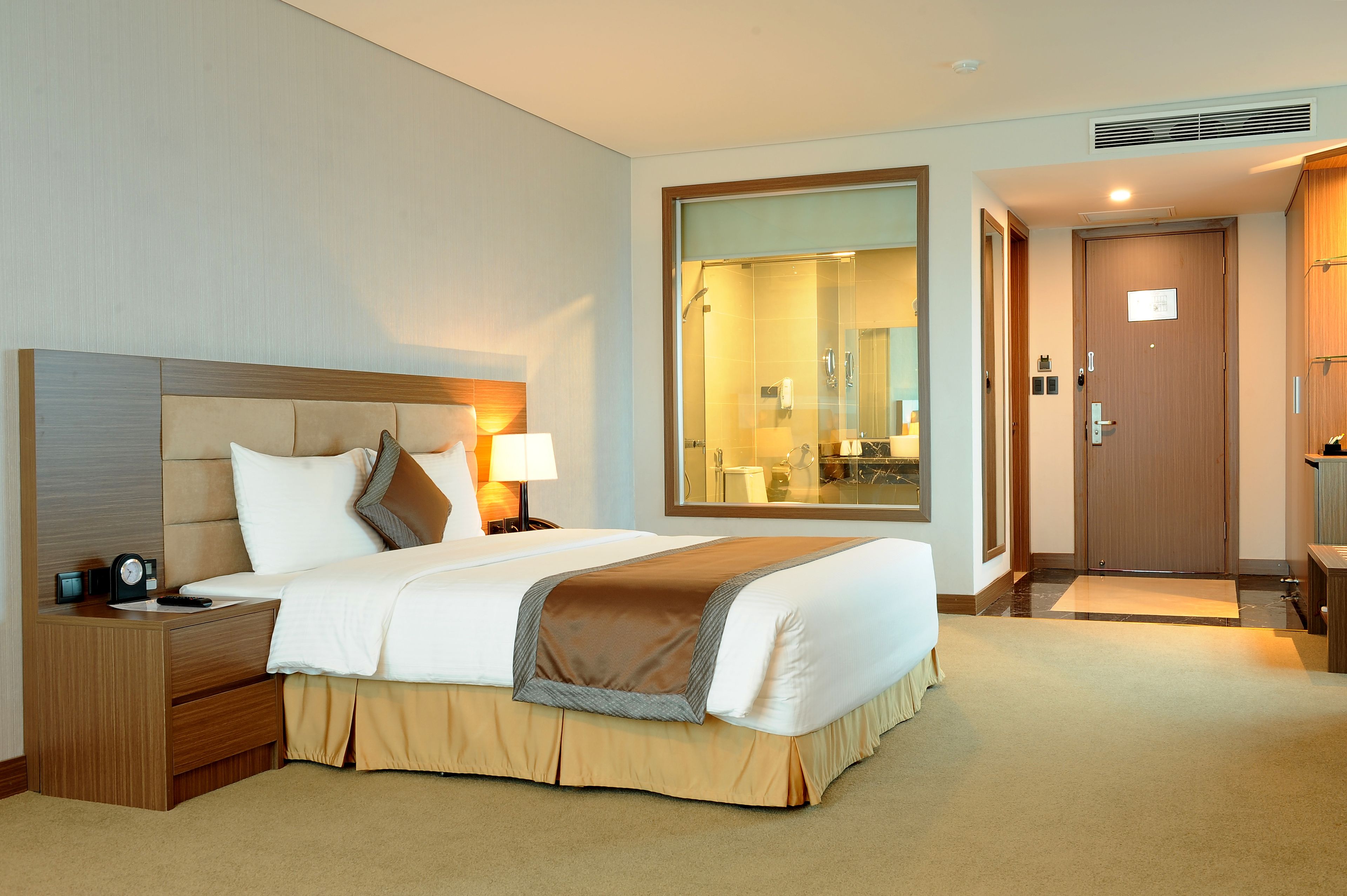 Een hotelkamer met een groot bed, een nachtkastje, een lamp, een spiegel en een deur naar een badkamer.