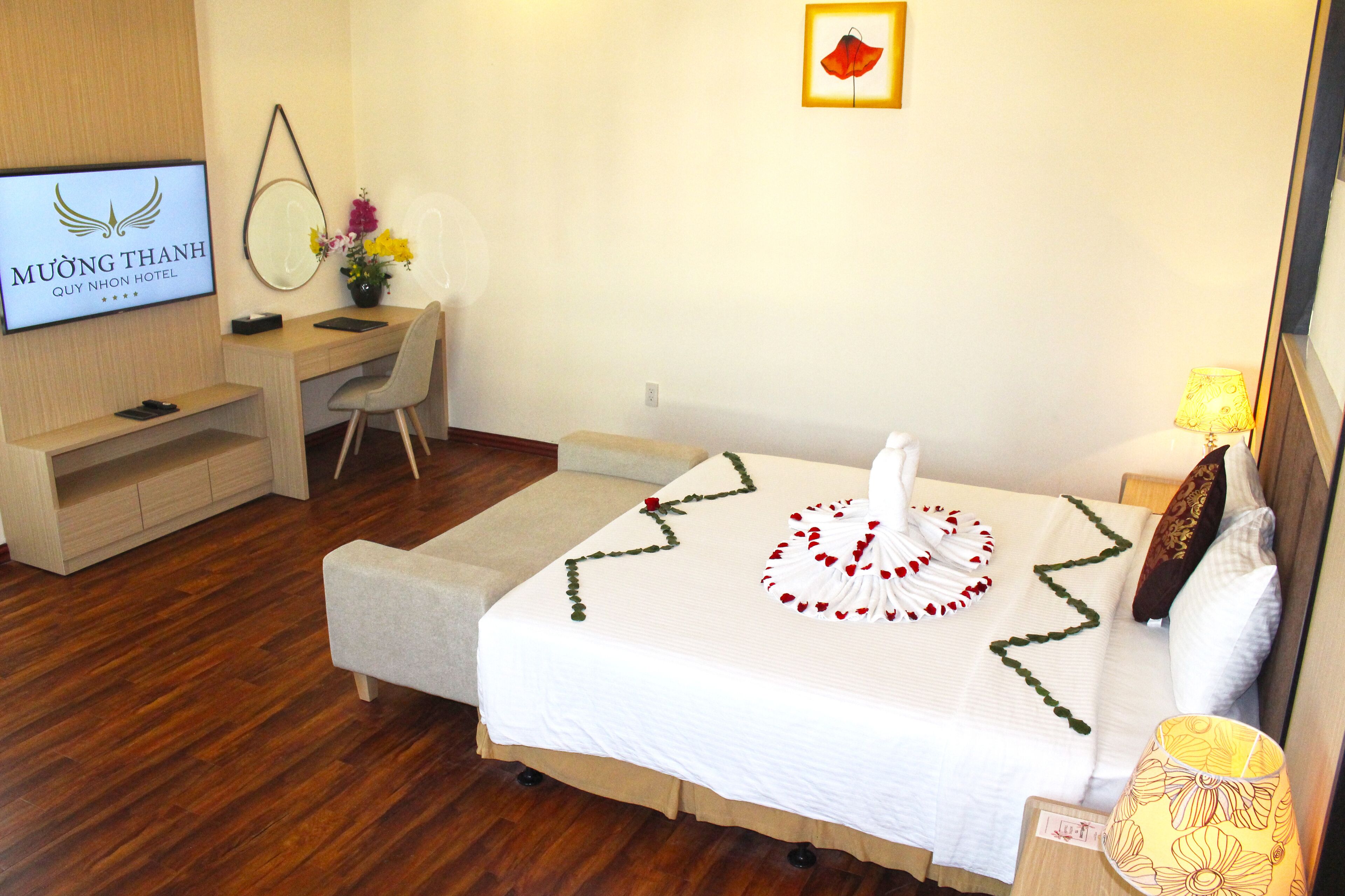 A hotel room with a bed, a desk, a chair, a TV, and a wall-mounted mirror.