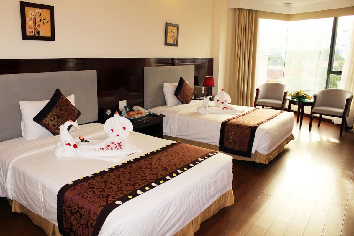 A hotel room with two beds, a sitting area with a chair and a table, and a view of the outside.