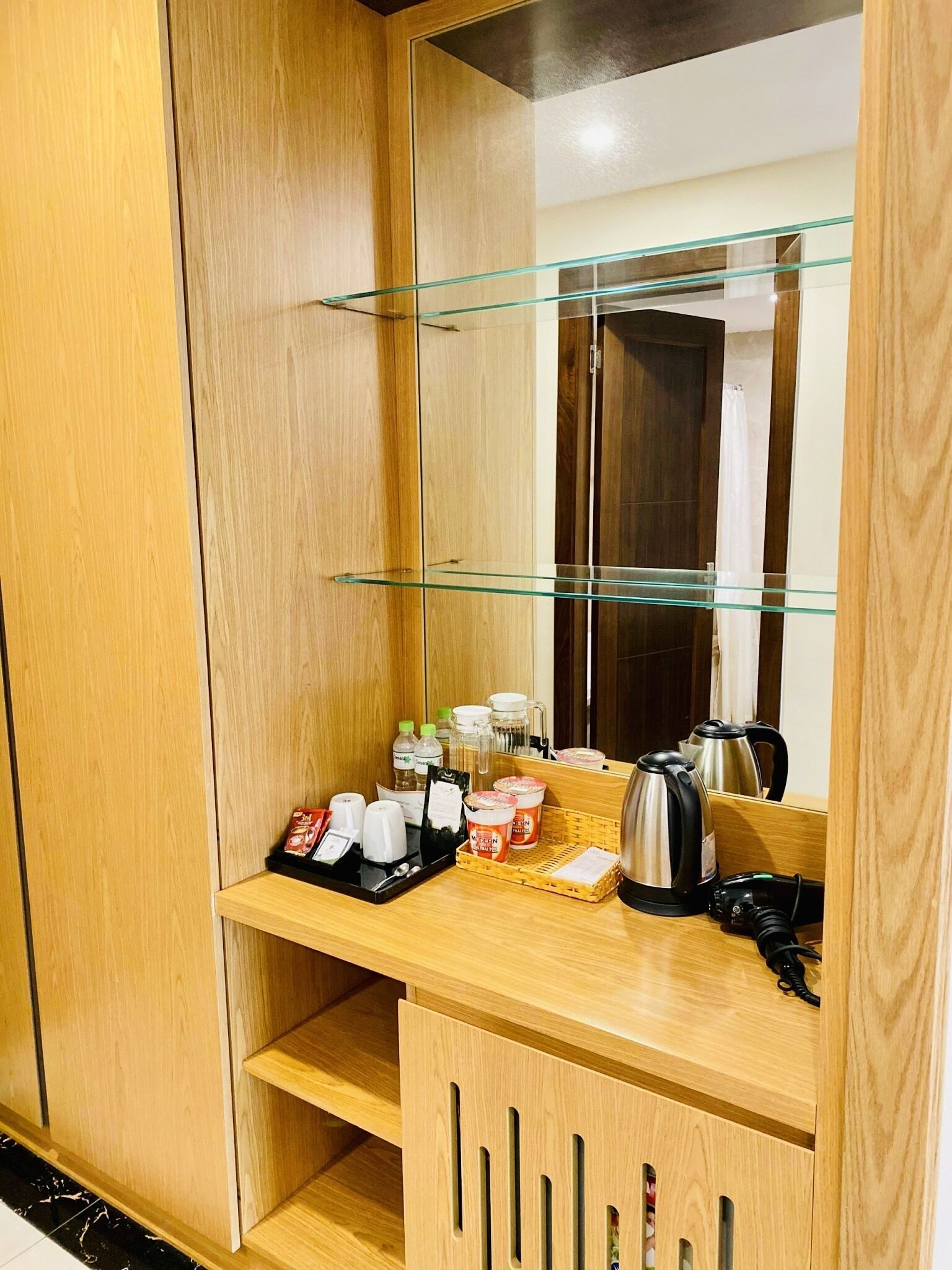Habitació d'hotel amb un armari de fusta, una prestatgeria de vidre amb productes de tocador, una paperera i una estació de càrrega.