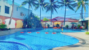 Ein Swimmingpool mit klarem, blauem Wasser, umgeben von Palmen und einem Gebäude mit rotem Dach.