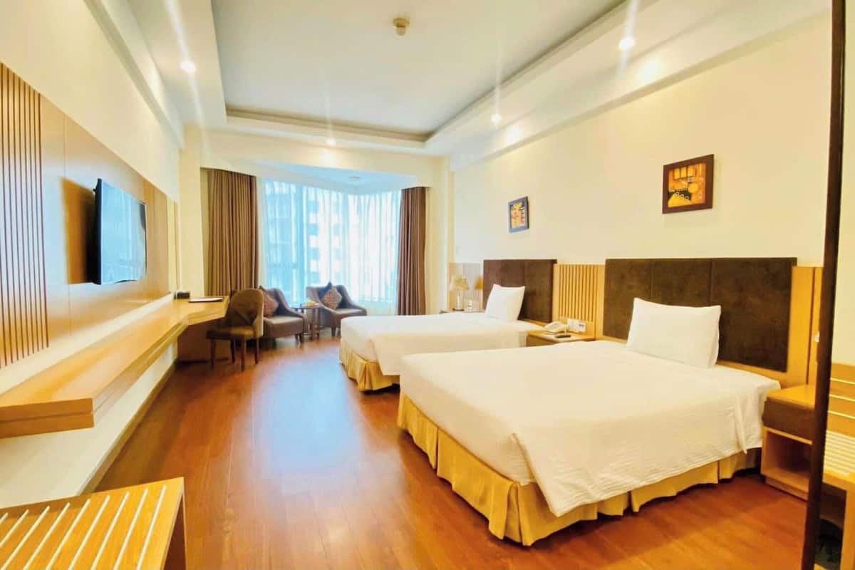 A hotel room with two beds, a desk, a chair, a TV, and a window with curtains.