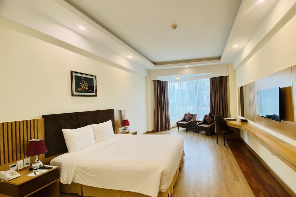 A hotel room with a large bed, a desk with a TV, a chair, and a window with curtains.