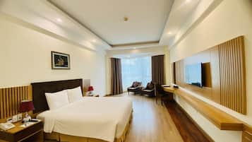 A hotel room with a large bed, a desk with a TV, a chair, and a window with curtains.