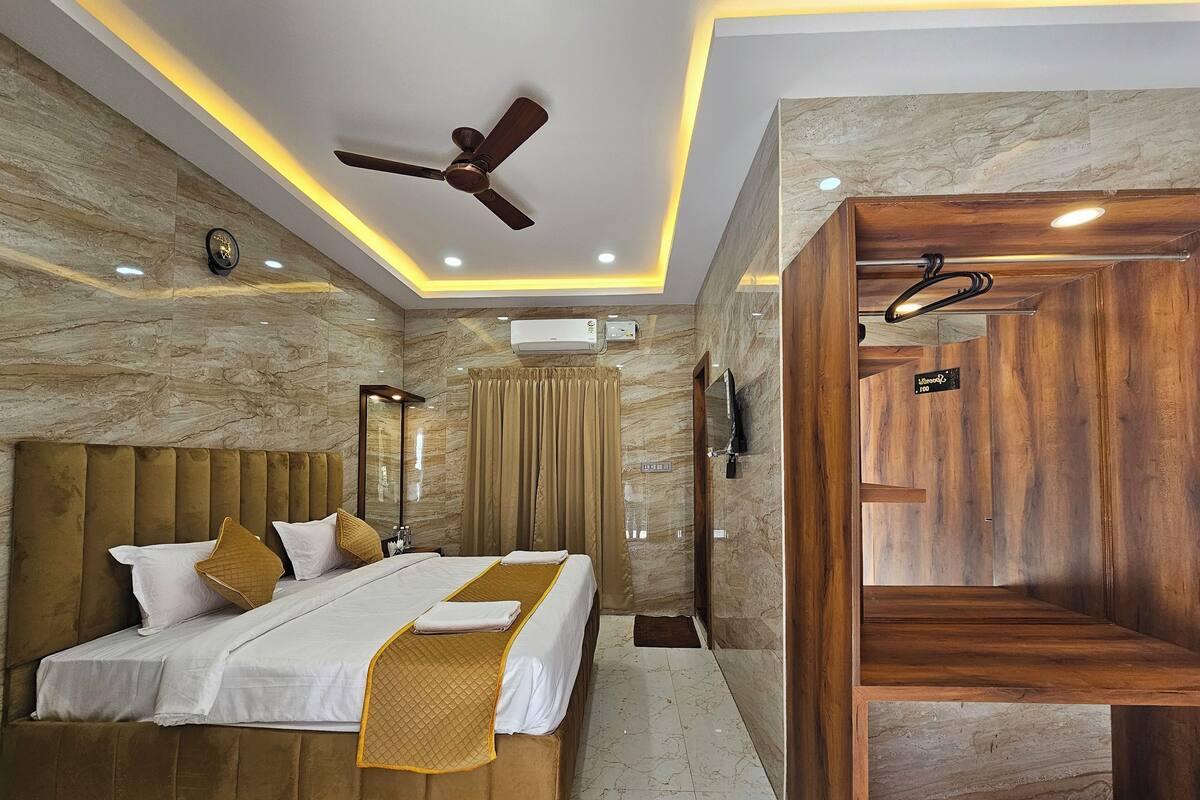 A modern hotel room with a large bed, a ceiling fan, marble walls, and a wooden vanity.