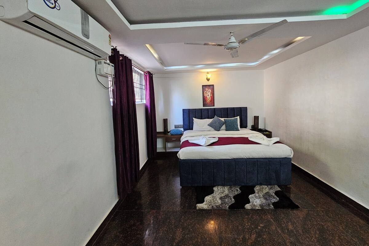 A hotel room with a bed, a ceiling fan, a nightstand, a lamp, and a window with curtains.