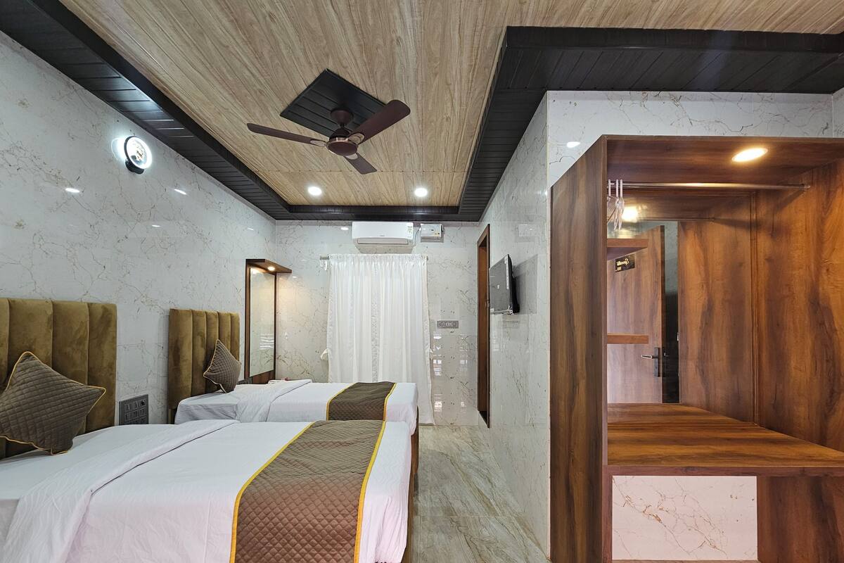 A hotel room with two beds, a ceiling fan, marble walls, and wooden accents.