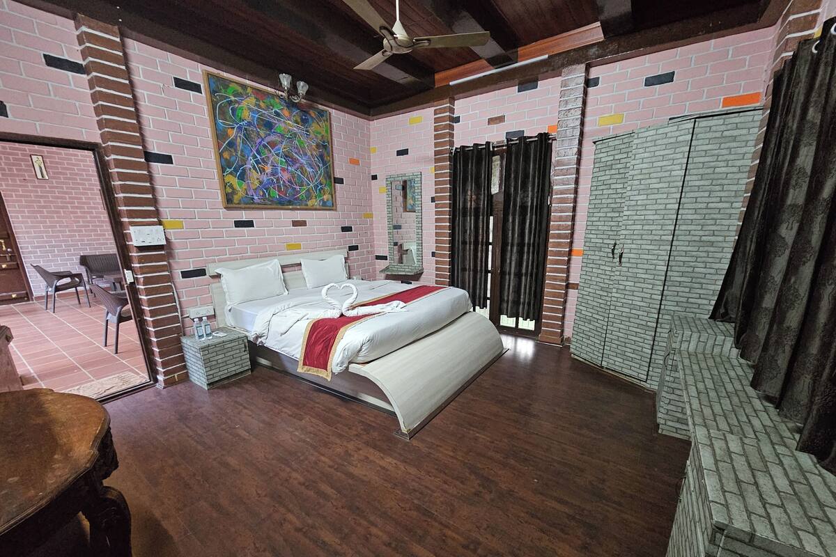 A hotel room with a brick-patterned wall, a large abstract painting, a bed with a heart-shaped towel, and a ceiling fan.