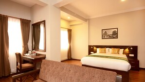 Habitación de hotel con cama, escritorio, silla y un amplio ventanal con cortinas.