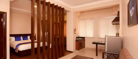 Quarto de hotel com cama, divisória de madeira, cozinha compacta, sofá e mesa.