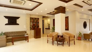 Un hall con sofá, sillones, una mesa de centro, mostrador de recepción y una planta en maceta.