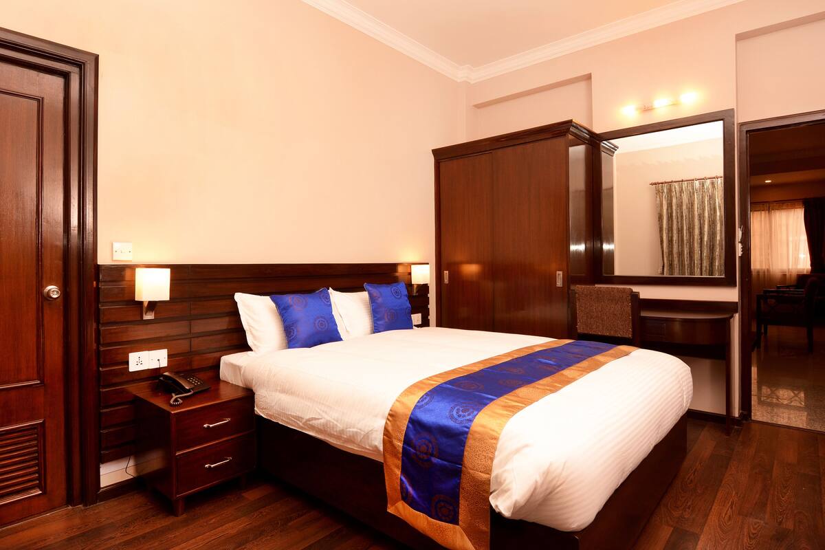 A hotel room with a large bed, wooden headboard, bedside tables, a desk, and a mirror.