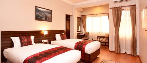 A hotel room with two beds, a desk, a chair, and a window with curtains.
