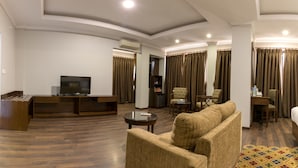 Habitación de hotel con una unidad de entretenimiento de madera, televisor de pantalla plana, sofá, mesa de centro y un pequeño escritorio con silla.
