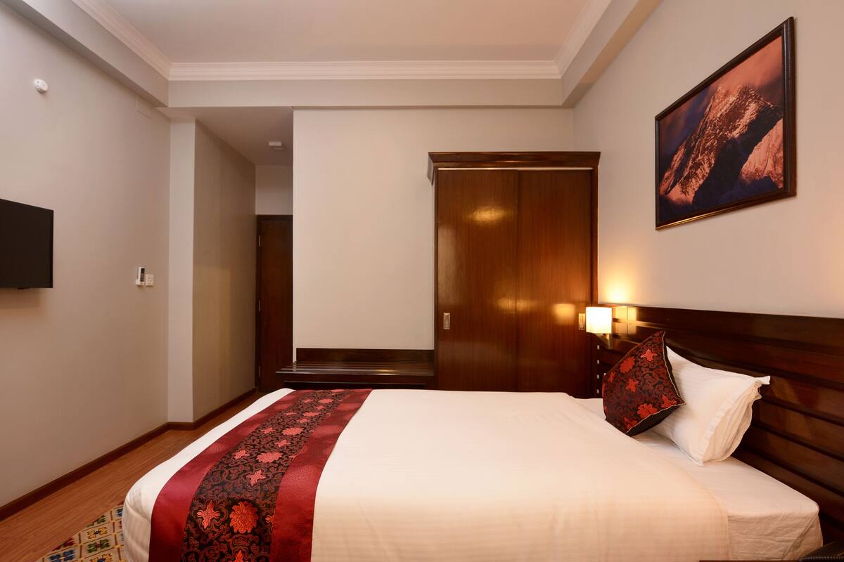 A hotel room with a large bed, a wooden headboard, a mounted TV, and a painting on the wall.