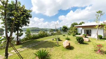 A modern house with a stone pathway leading to a door, surrounded by lush greenery and a lake view.
