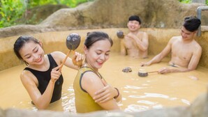 A group of people in a hot spring bath area with a natural stone wall and greenery in the background. - Muong Thanh Luxury Dien Lam Hotel (Hung Chau)