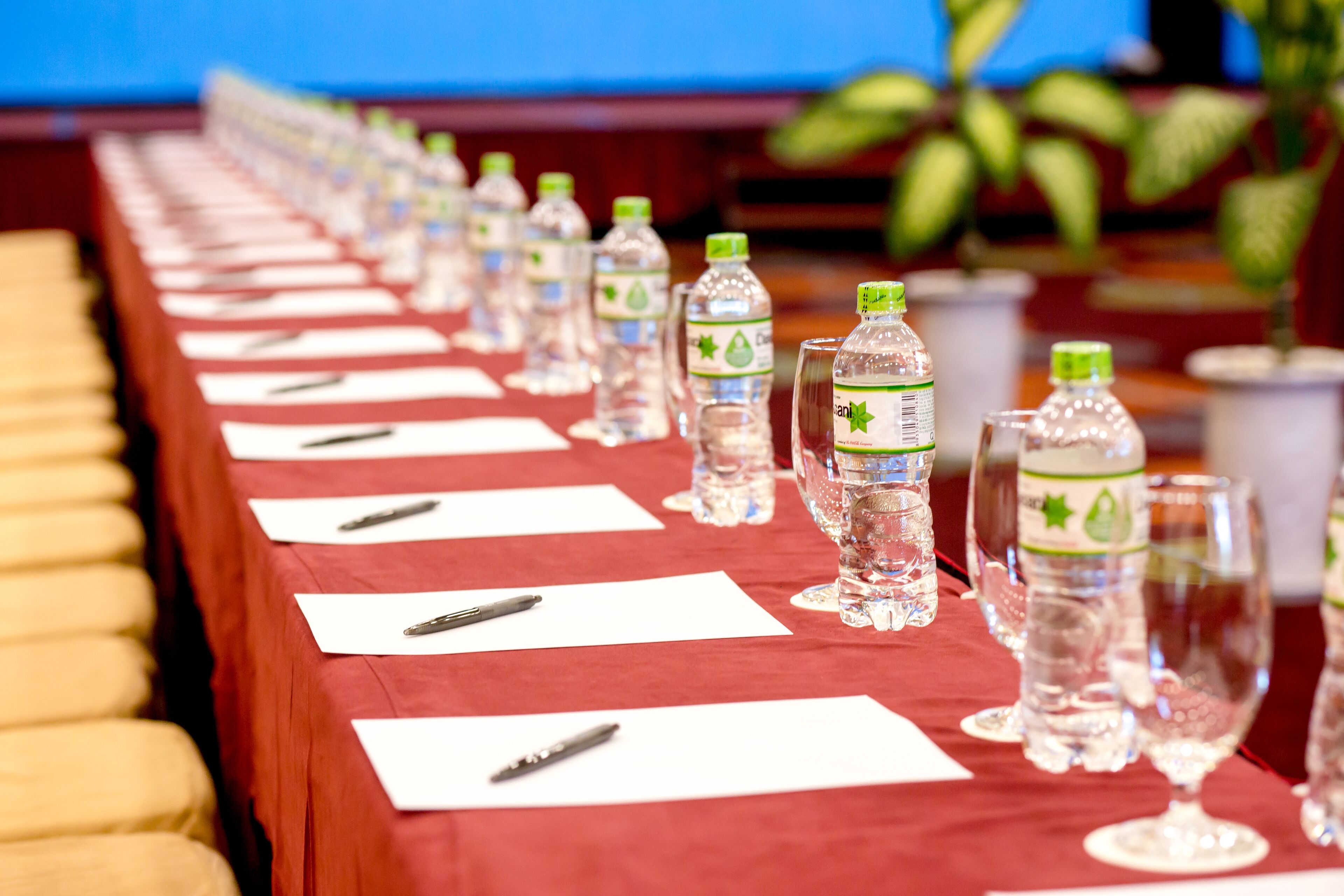 A conference table with water bottles and glasses, lined with white notepads and pens.