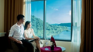 A couple sitting by a window with a view of a lake and hills. - Muong Thanh Luxury Dien Lam Hotel (Hung Chau)