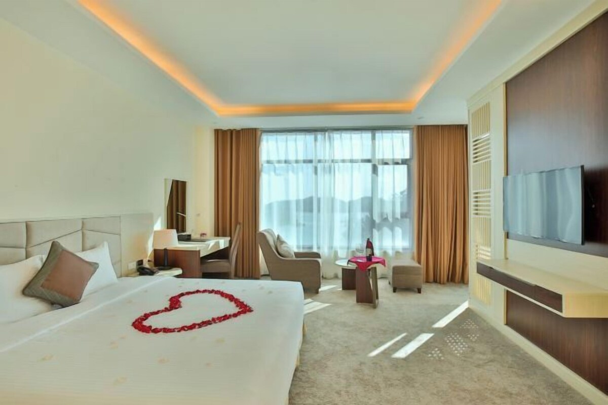 Ein Hotelzimmer mit einem großen Bett, einem Schreibtisch, einem Sessel, einem Fernseher und Blick auf die Stadt.