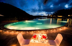 A round outdoor pool with a table set for two, surrounded by lights and chairs. - Muong Thanh Luxury Dien Lam Hotel (Hung Chau)