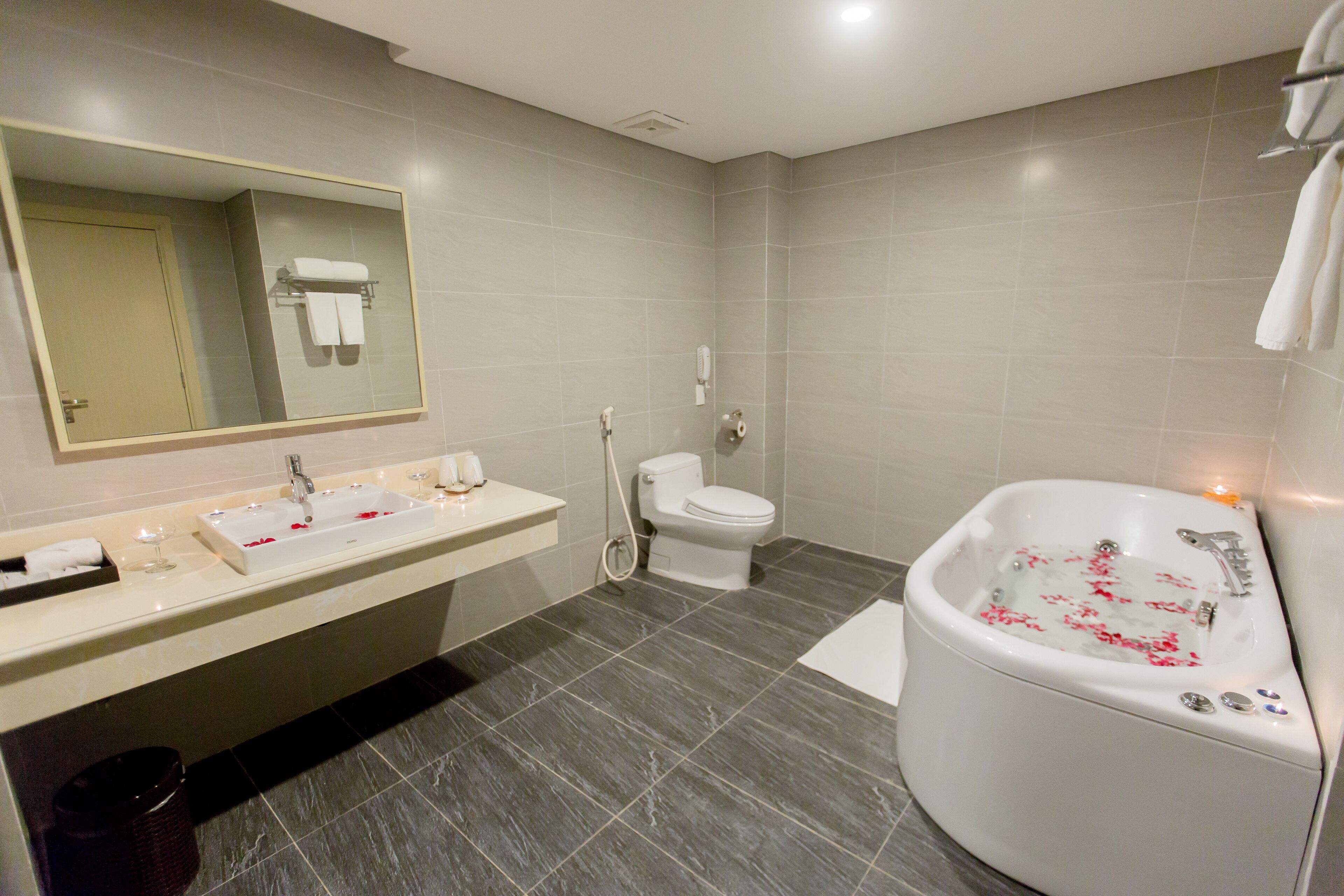 Een moderne badkamer met een grote spiegel, een wastafel, een toilet en een badkuip met rozenblaadjes.