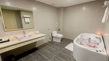 Een moderne badkamer met een grote spiegel, een wastafel, een toilet en een badkuip met rozenblaadjes.